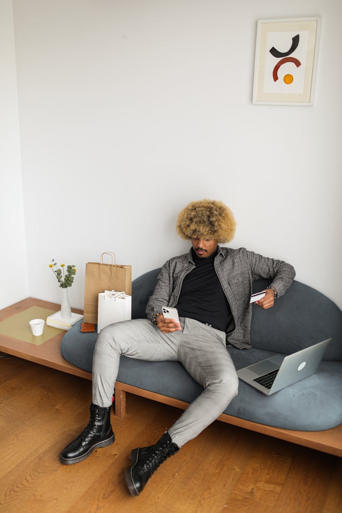 Afro-haired man shopping online with credit card and laptop in a stylish room.