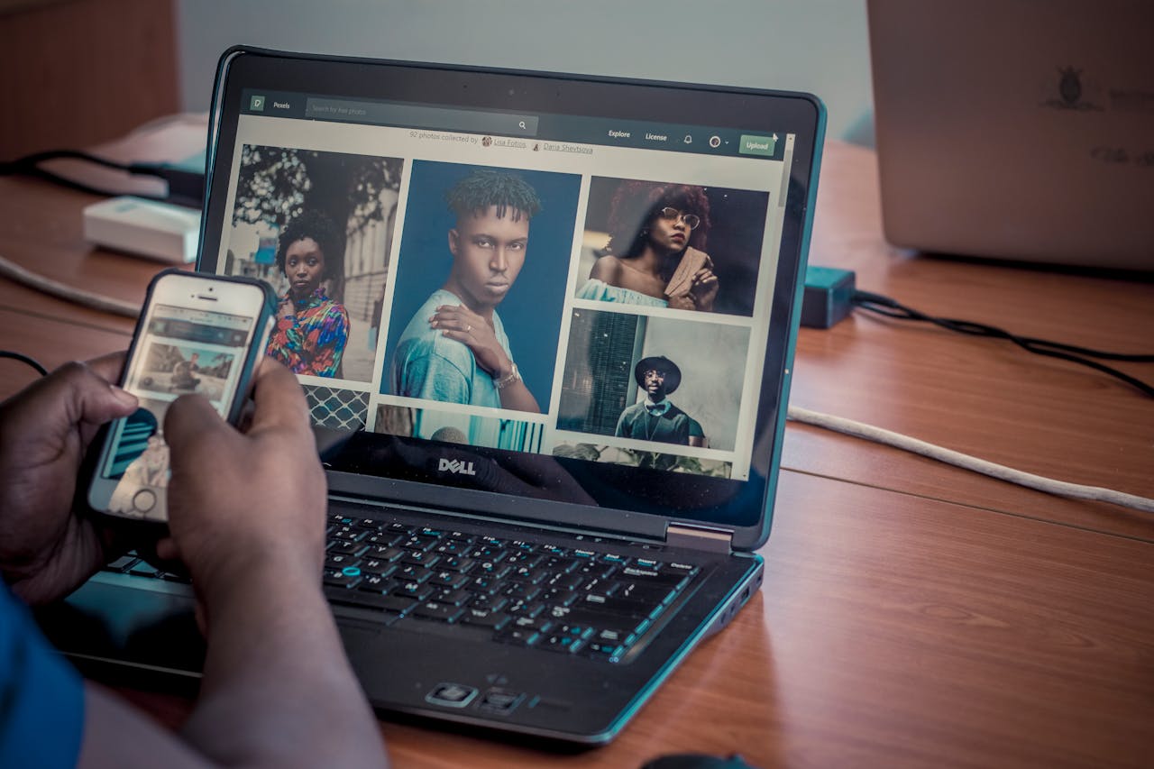 A person viewing portrait photos on a Dell laptop and smartphone, indoors.